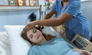 Pielęgniarka bada pacjentkę leżącą w łóżku szpitalnym.