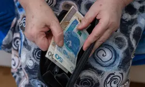Dłonie wkładają polskie banknoty 50 i 200 zł do czarnego portfela.