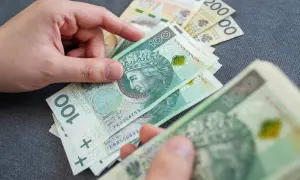 Dłoń trzyma polskie banknoty 100 zł i 200 zł.