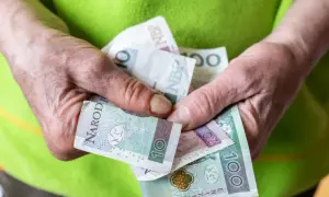 Dłonie starszej osoby trzymają polskie banknoty: 10, 20 i 100 zł.