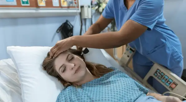 Pielęgniarka bada pacjentkę leżącą w łóżku szpitalnym.